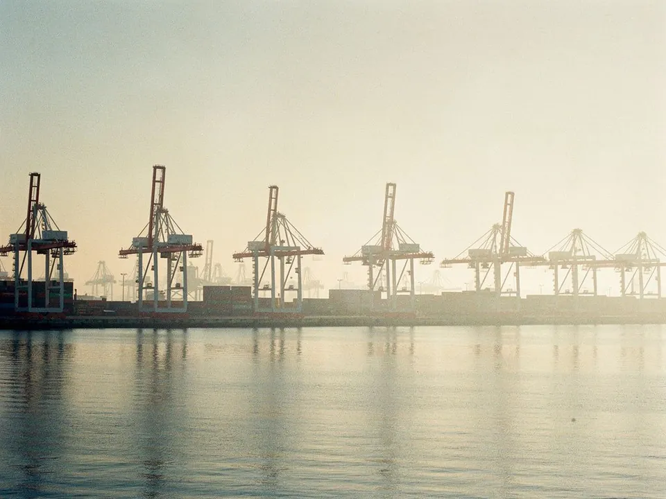 Port cranes silhouetted in morning haze over calm water